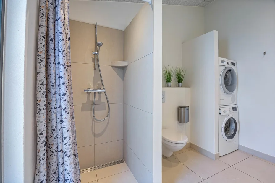 Un baño con ducha, inodoro y lavadoras apiladas.