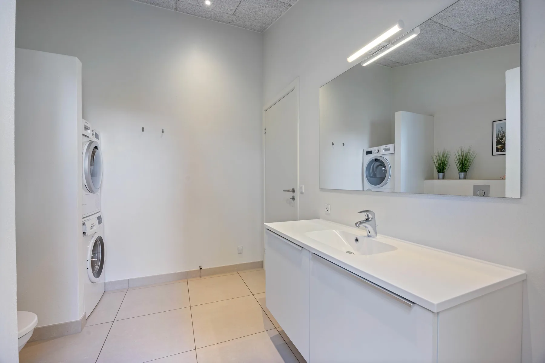 Un baño luminoso tiene un mueble largo con lavabo y un espejo grande.