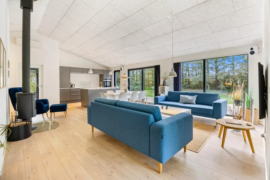 Una sala de estar luminosa y diáfana, con asientos azules y un comedor junto a grandes ventanales.