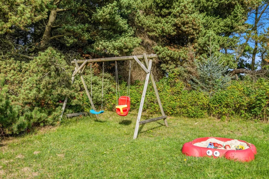 Una zona de juegos en el jardín con un columpio de madera y una pequeña piscina inflable.