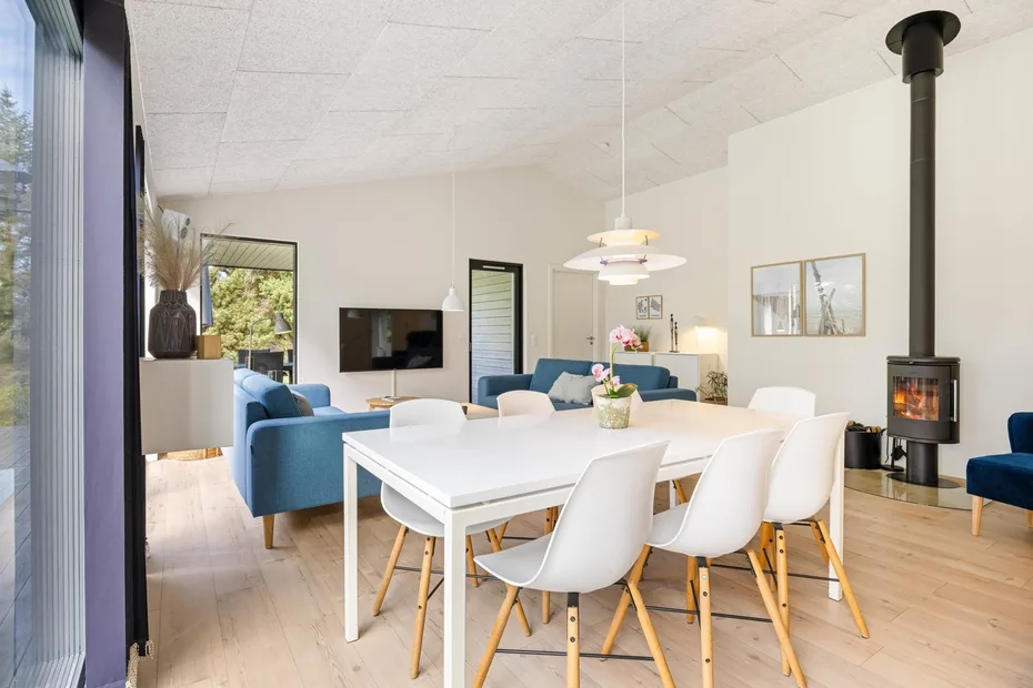 Una luminosa sala de estar y comedor diáfana tiene una mesa blanca y asientos azules.