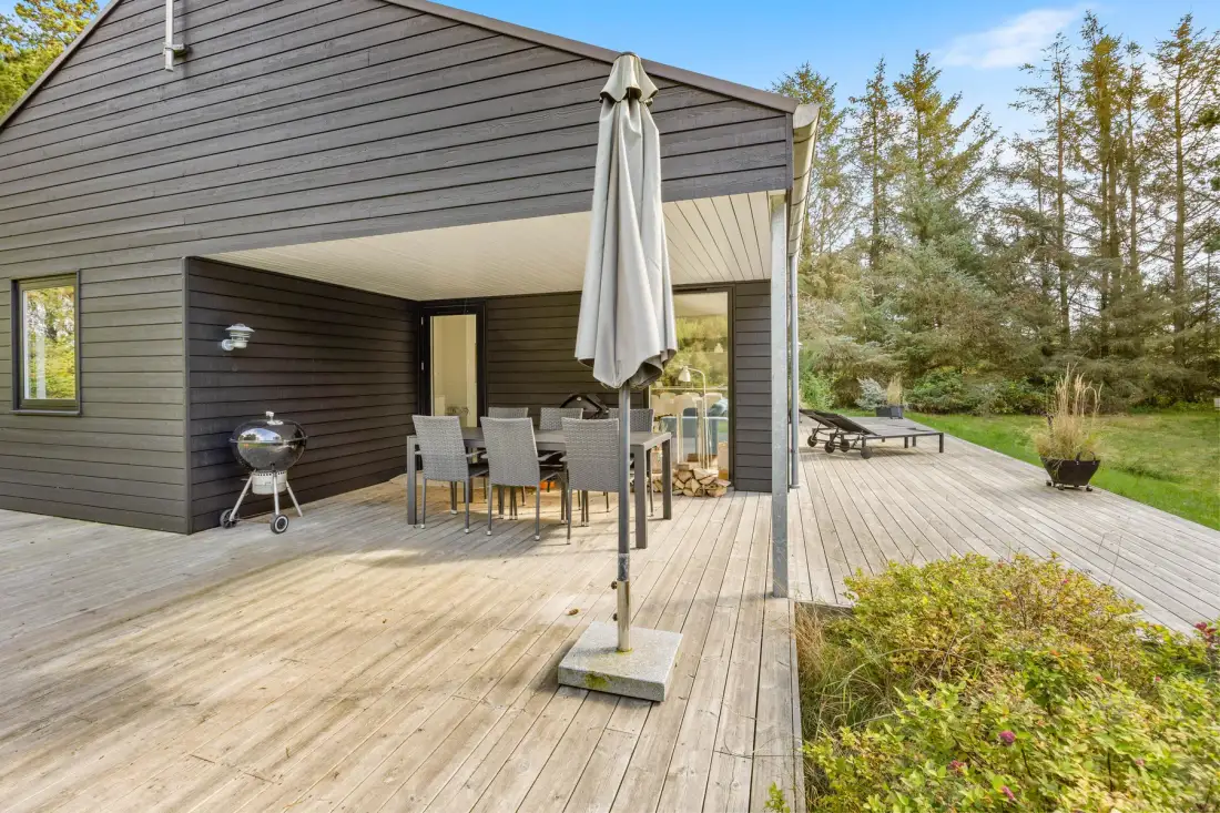 Una zona de comedor exterior cubierta da a una terraza de madera junto a la casa.