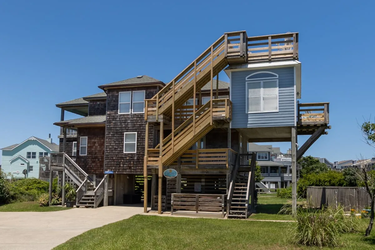 Una casa elevada de estilo costero con escaleras exteriores de madera y una terraza en la azotea.