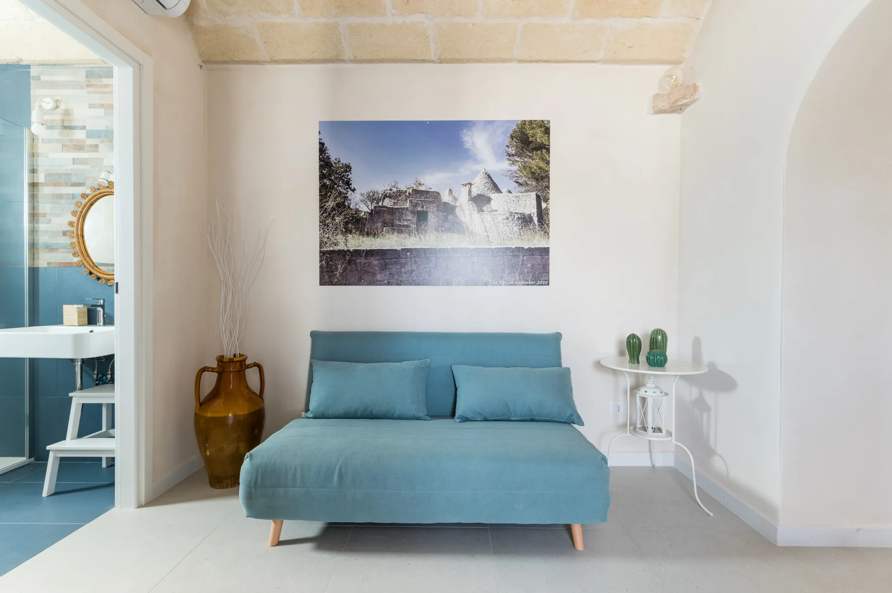 A bedroom with a blue bed beneath a framed landscape picture.