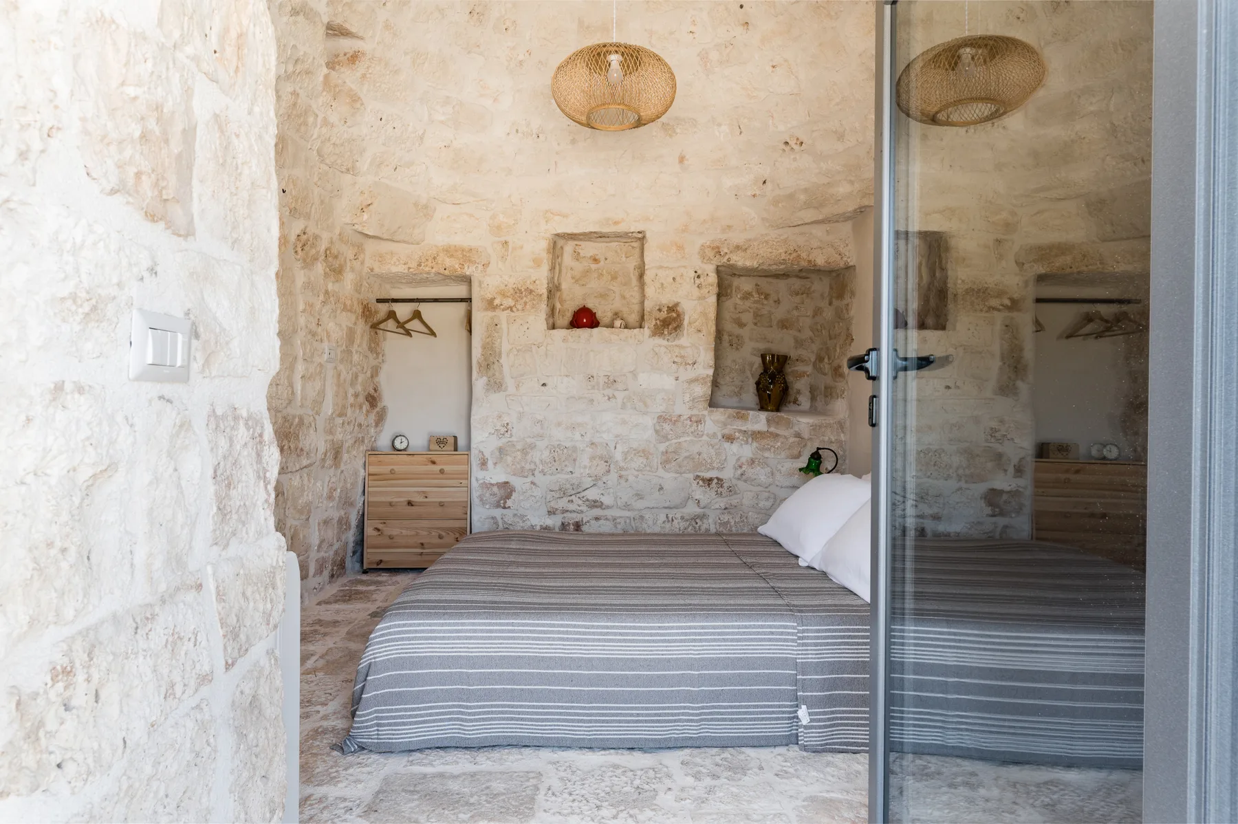 A bedroom with a striped bed, stone walls, and a glass door.