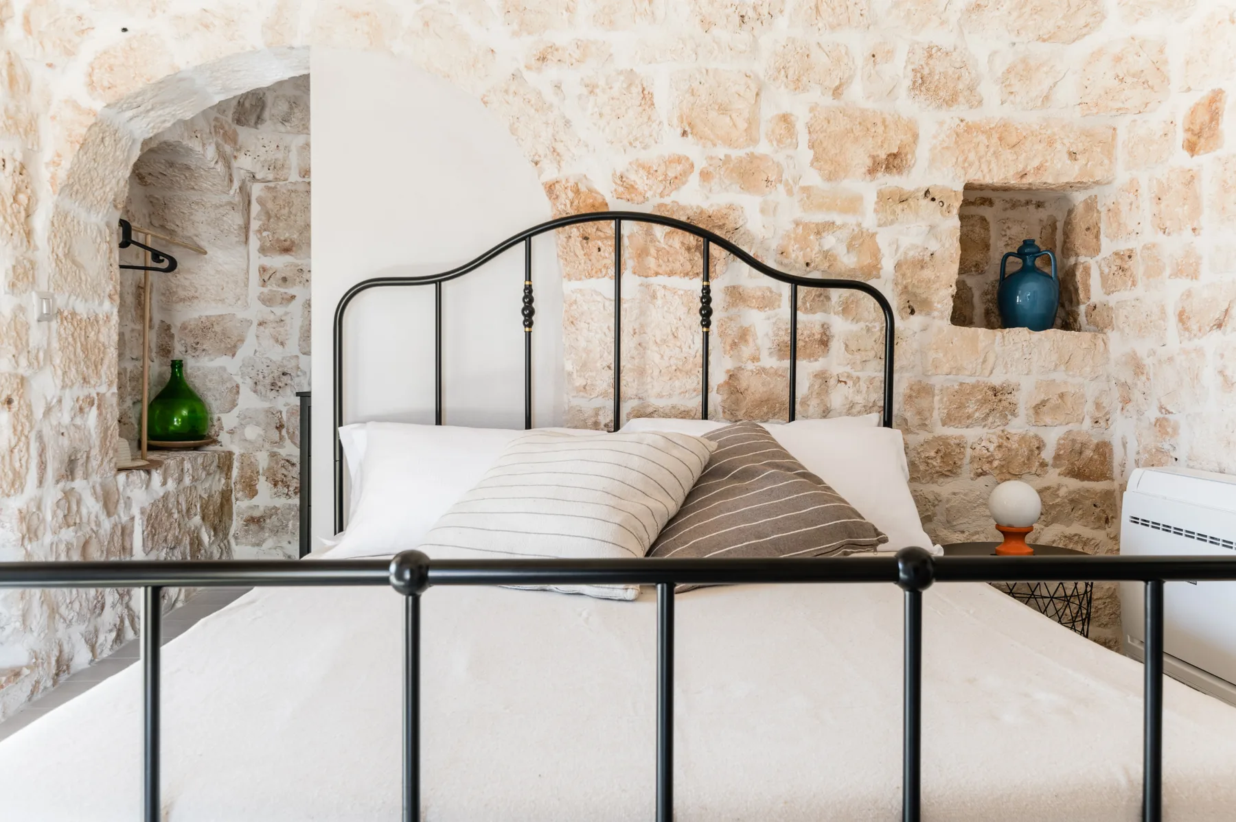 A bedroom with a metal bed frame and pillows against a stone wall.