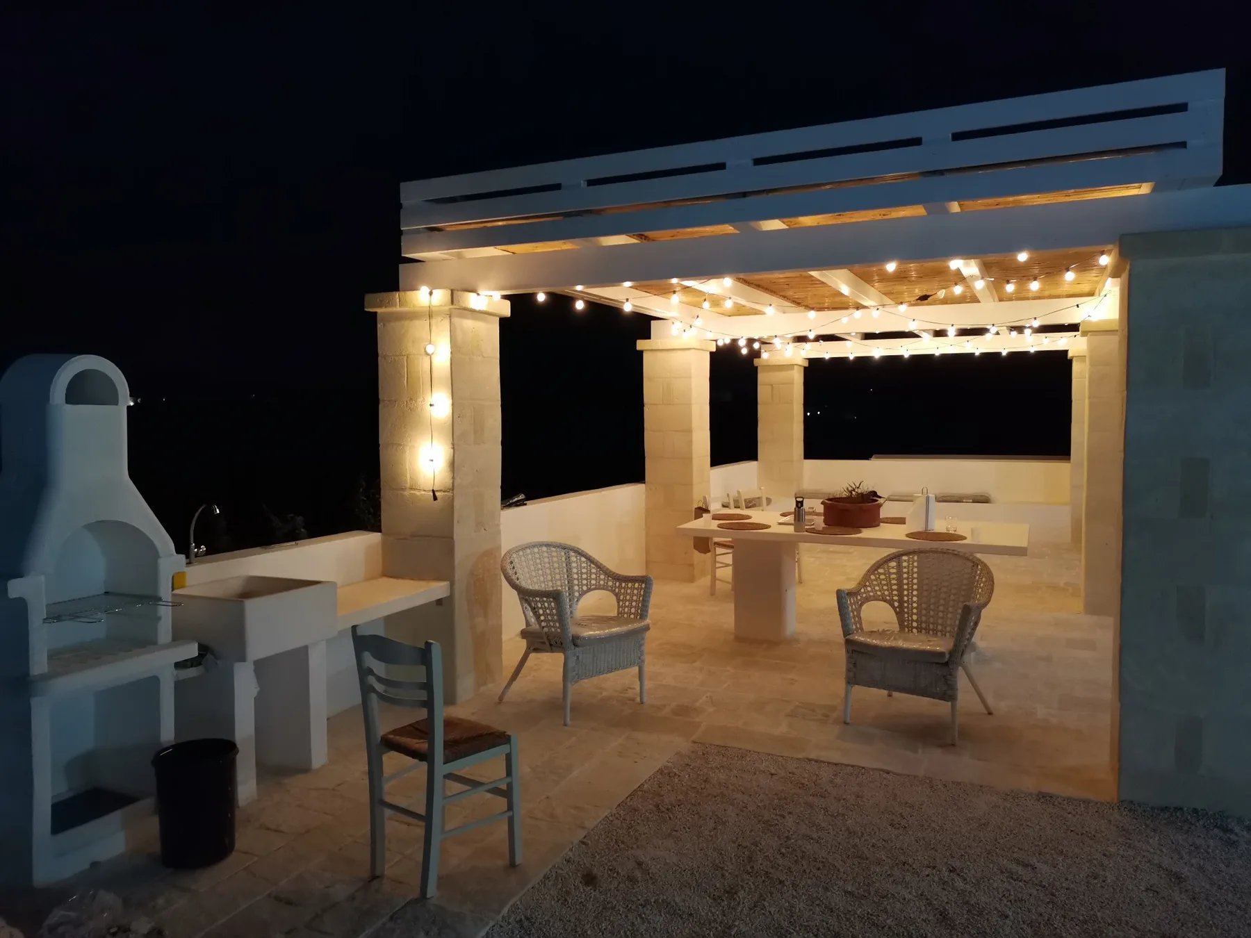 A lit outdoor pergola with a dining table and seating at night.