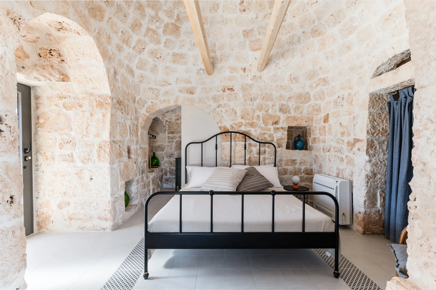 A bedroom with a black metal bed set against exposed stone walls.