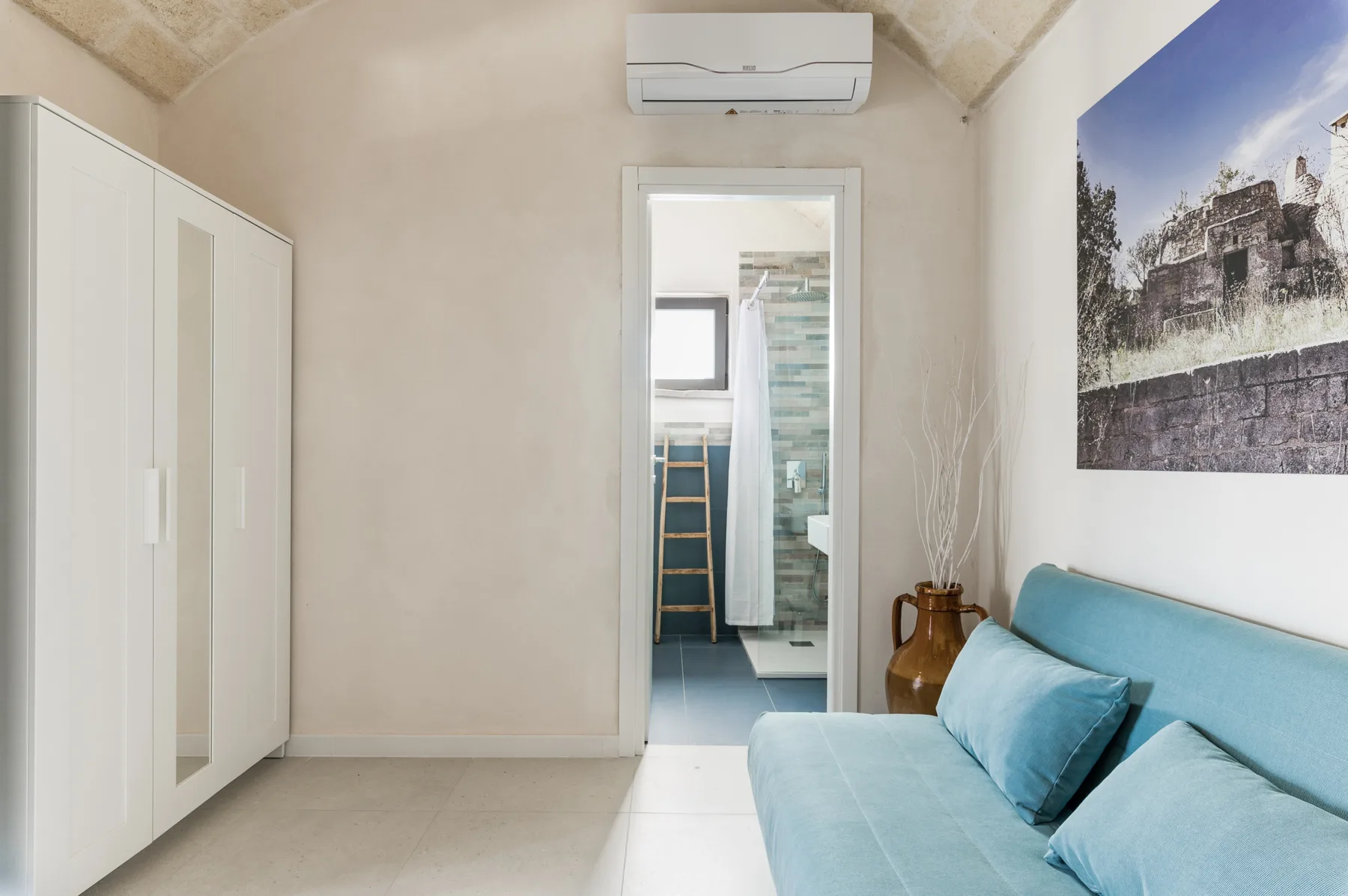 A bedroom with a blue bed, wardrobe, and doorway to a bathroom.