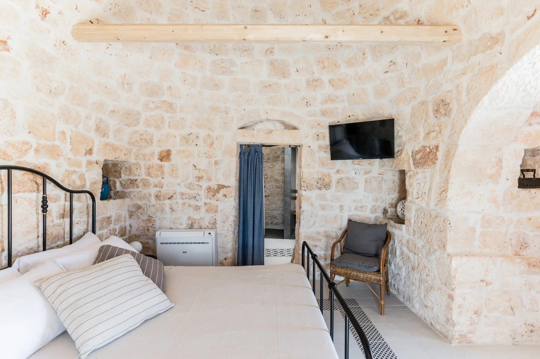 A stone bedroom with a bed, a curtained doorway, and a wall-mounted television.