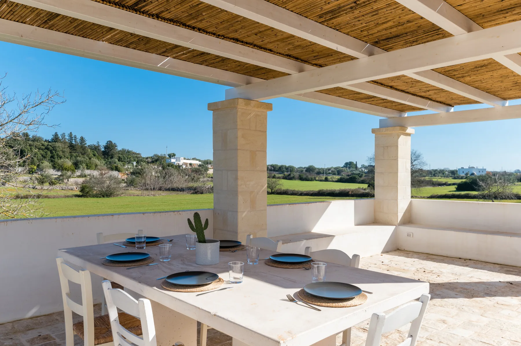 A covered outdoor dining area with a table overlooking green fields.