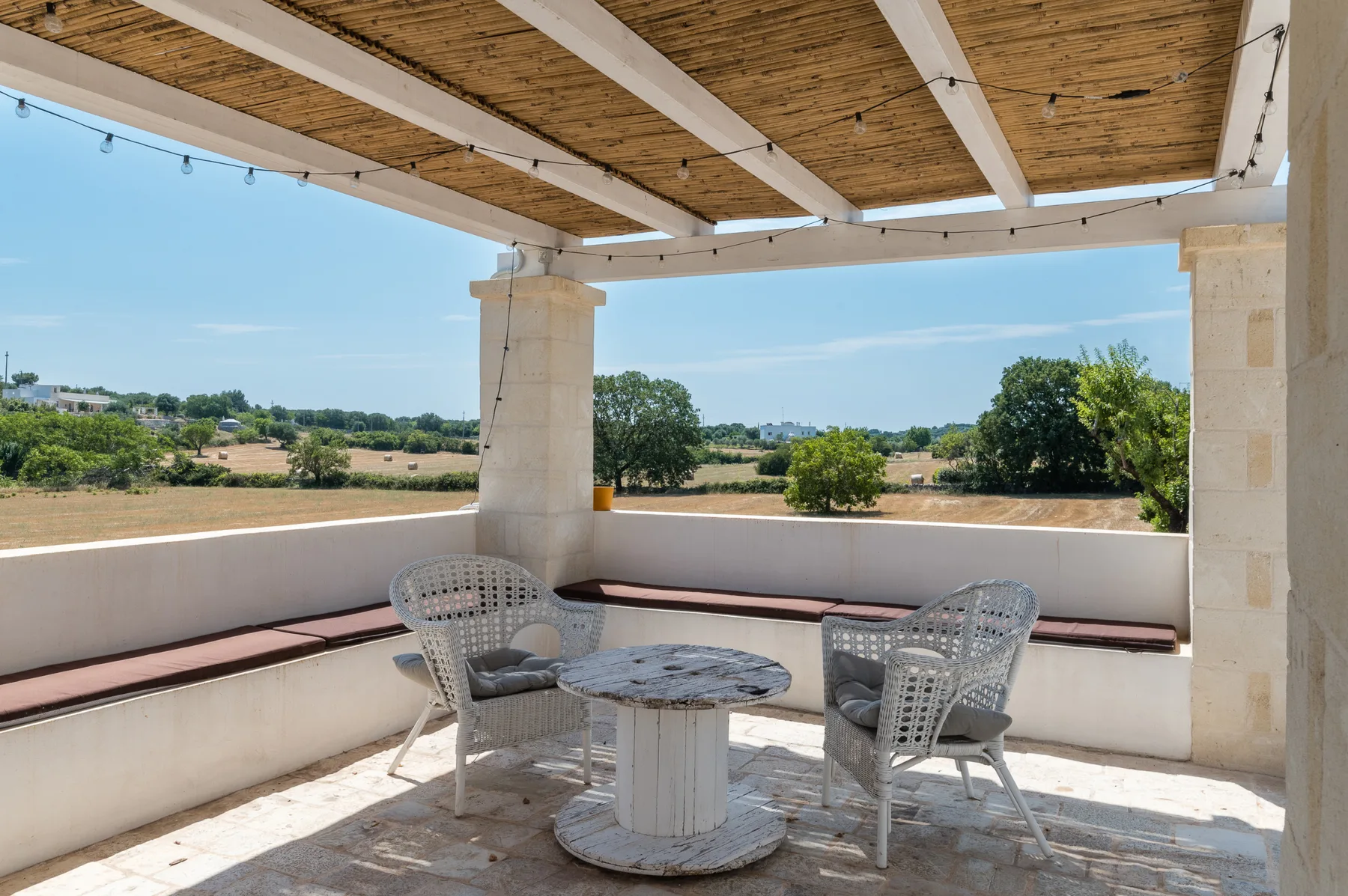 A covered outdoor terrace with seating and a table overlooking greenery.