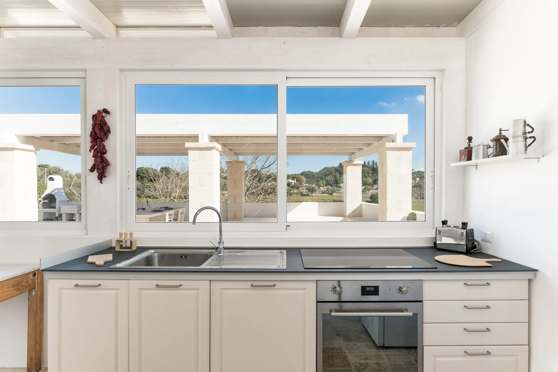A bright kitchen with a sink, countertop, and windows overlooking an outdoor patio.