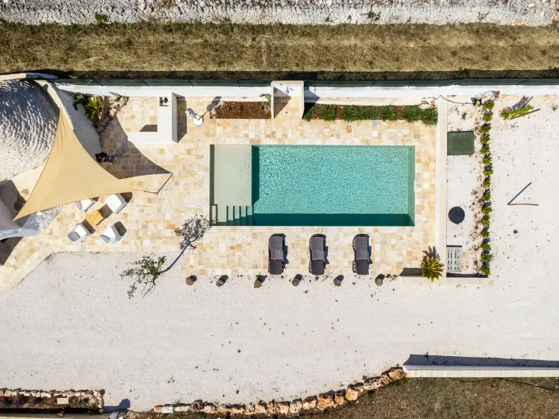 An aerial view of an outdoor pool beside a paved patio and sandy ground.