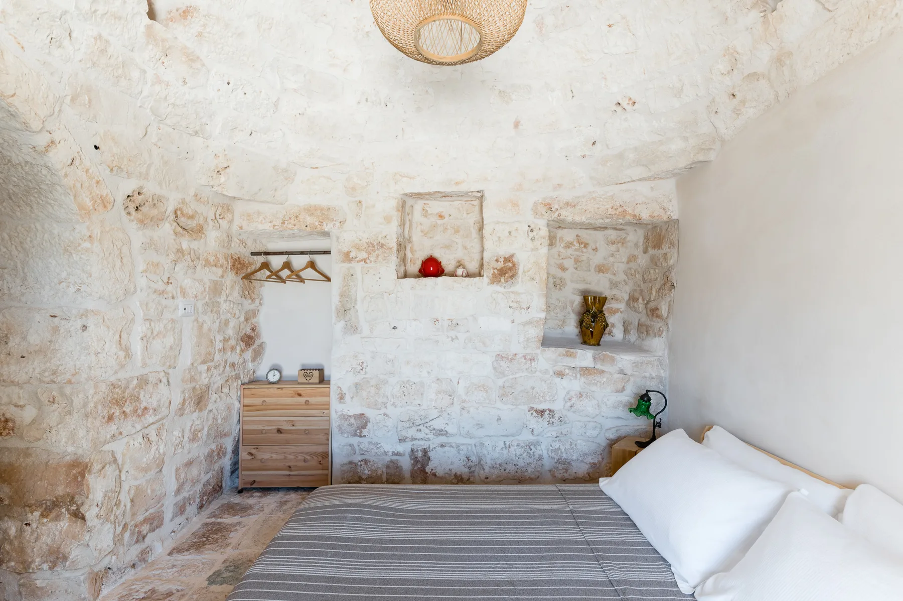 A bedroom with a bed, wooden drawers, and exposed stone walls.