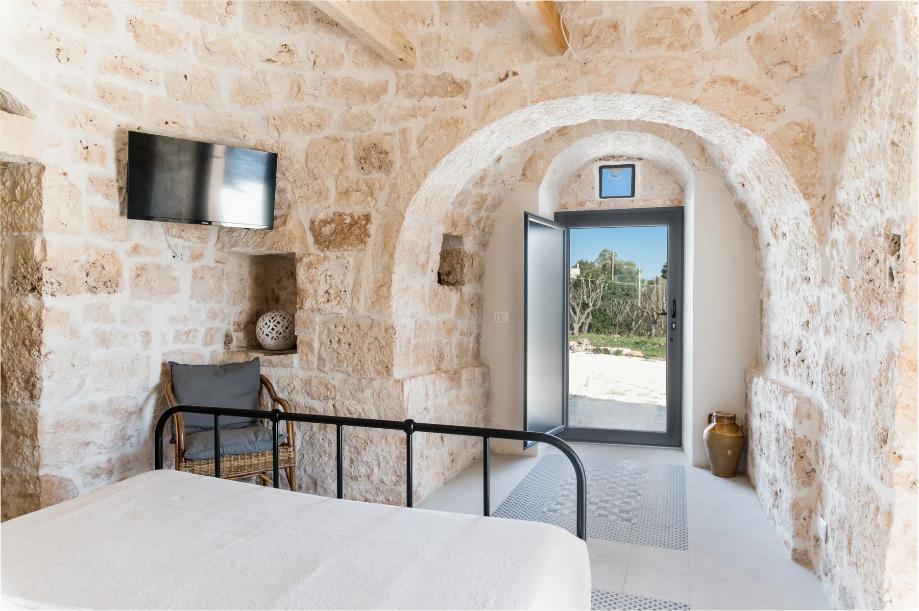 A stone bedroom with a black metal bed frame and an open doorway.