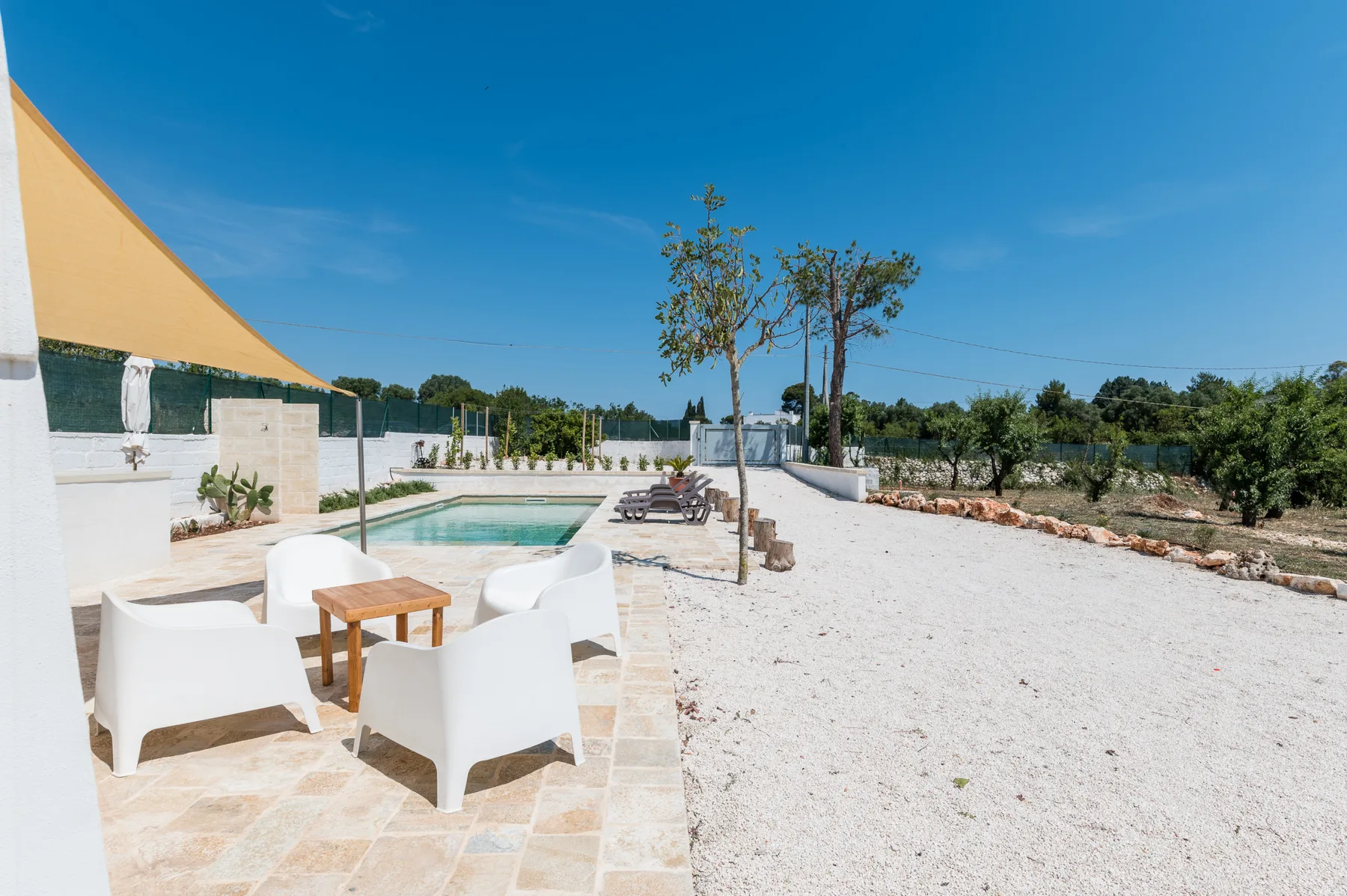An outdoor pool patio with white seating beneath a shade canopy.
