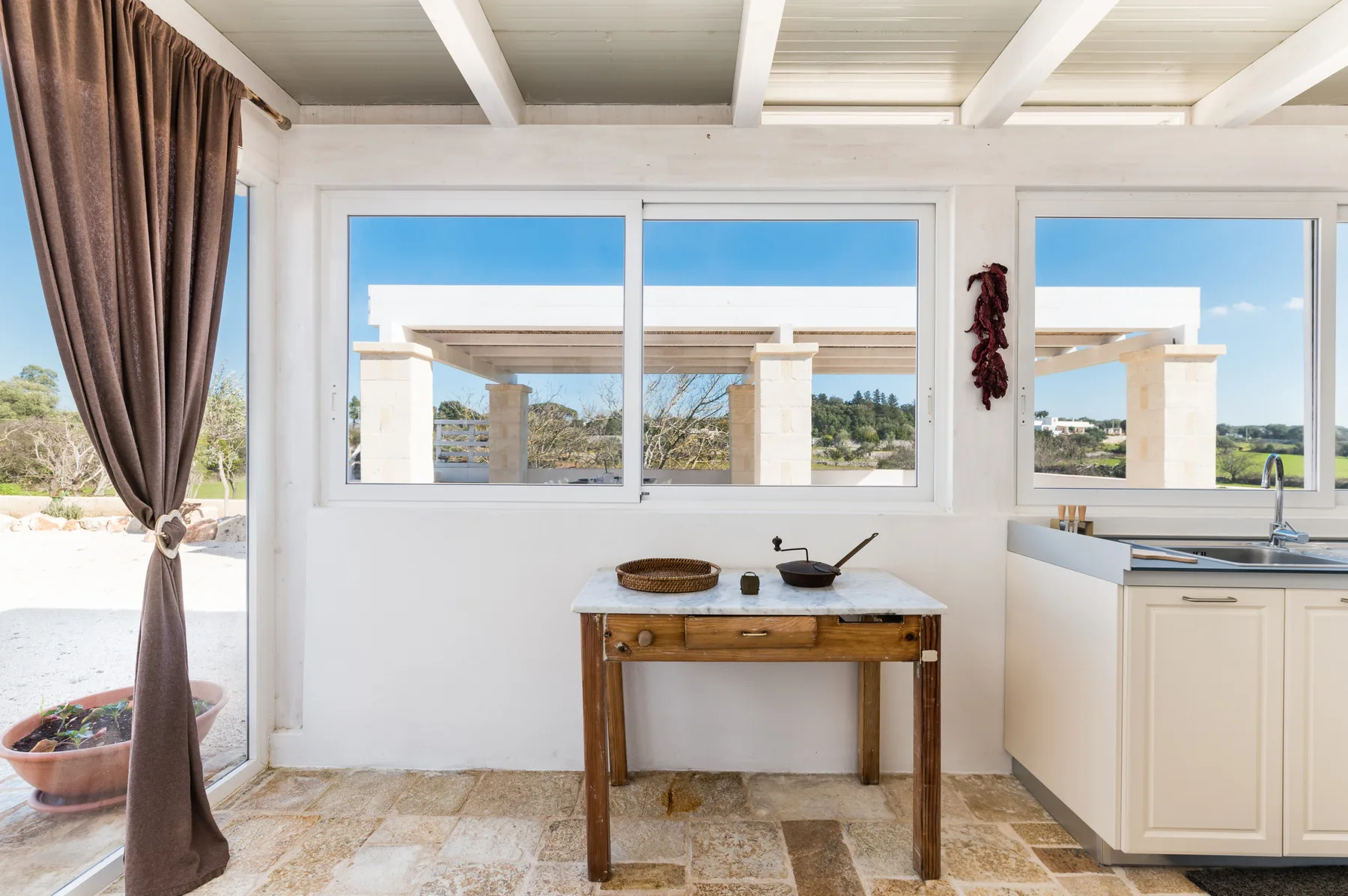 A bright kitchen area with a wooden table beneath wide windows.