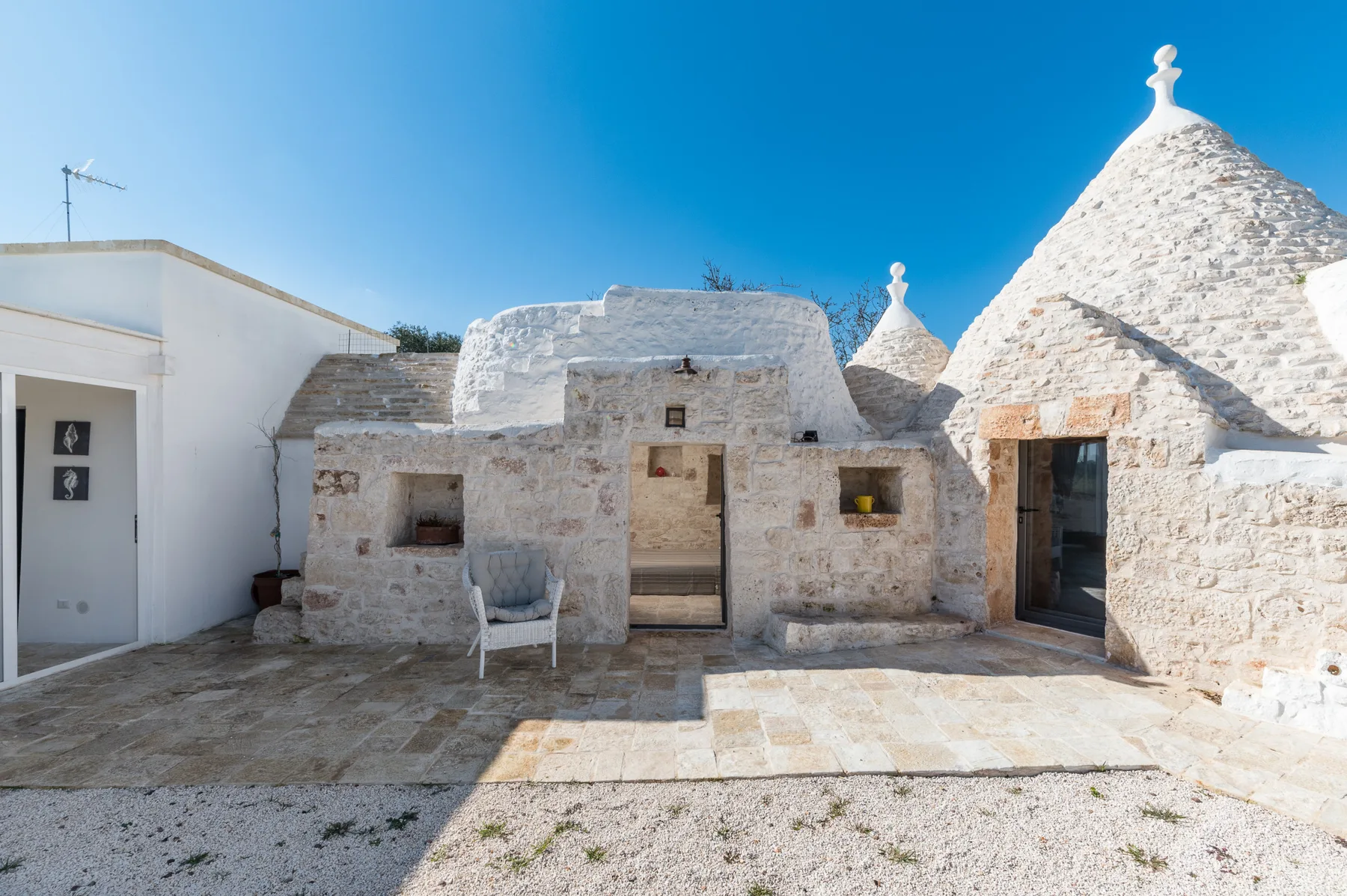 A sunlit stone courtyard with traditional conical-roofed buildings and a paved patio.