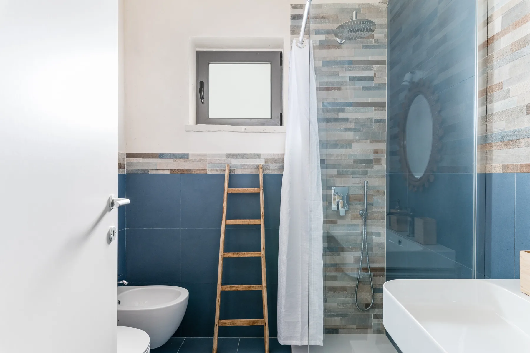 A tiled bathroom with a shower, toilet, and small window.