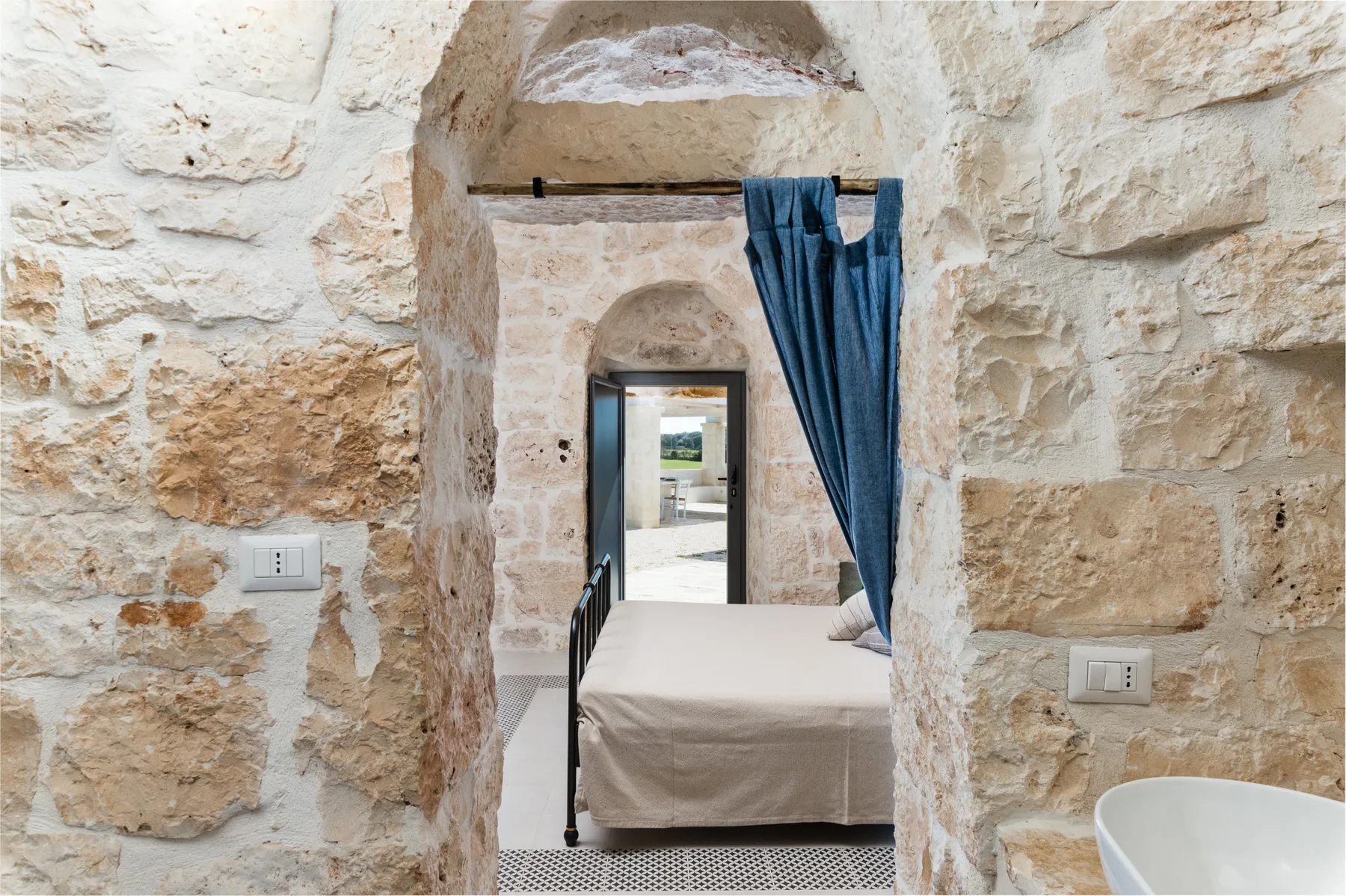 A bedroom with a bed set within a stone archway and a blue curtain.