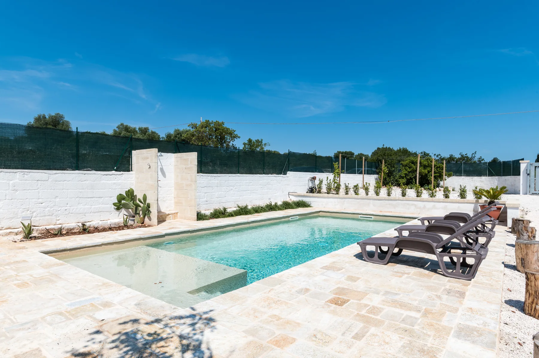 An outdoor swimming pool is surrounded by a pale stone patio and reclining loungers.