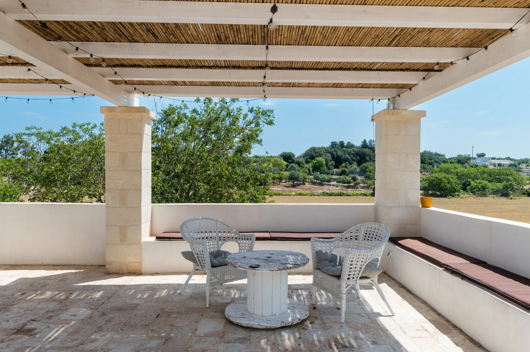 A covered outdoor terrace with wicker seating and a view of greenery.