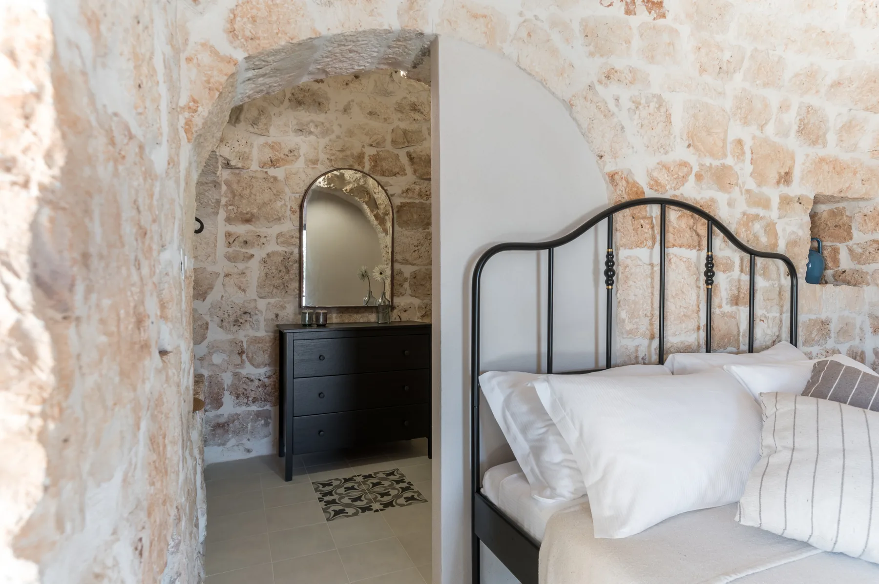 A bedroom with a black metal bed beside an arched stone doorway.