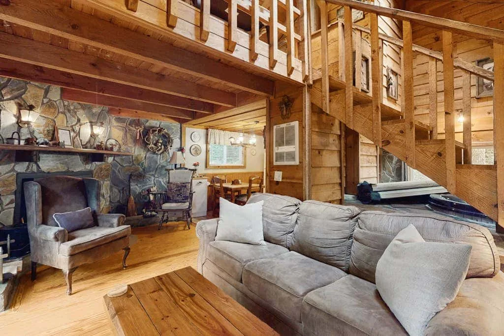 Una sala de estar revestida de madera con un sofá gris y una escalera al nivel superior.