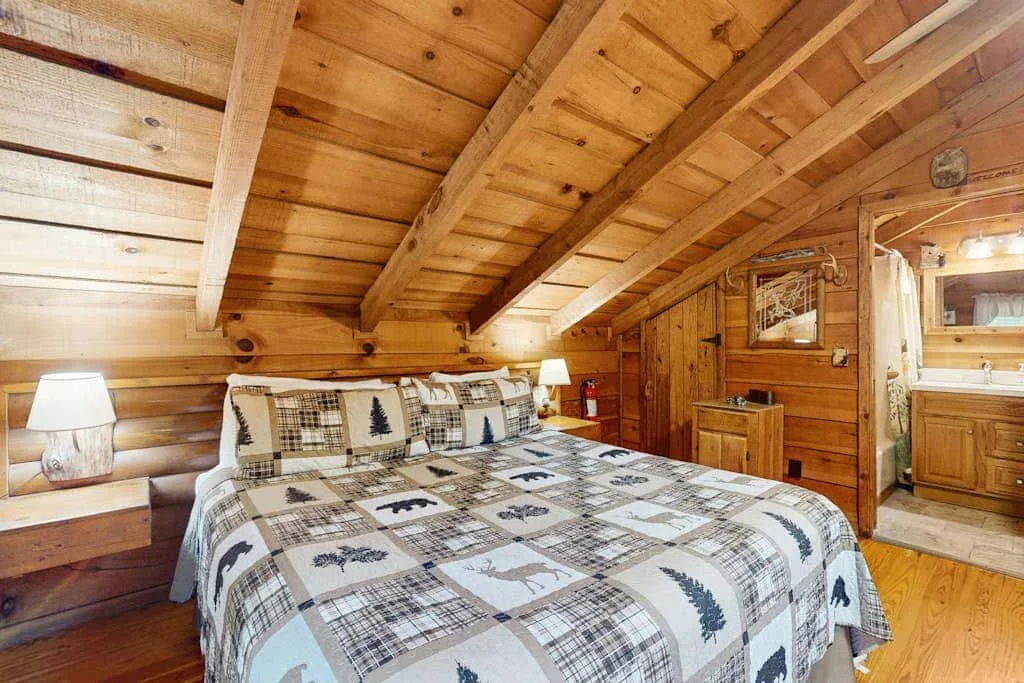 Un dormitorio con una cama estampada bajo un techo de madera inclinado.