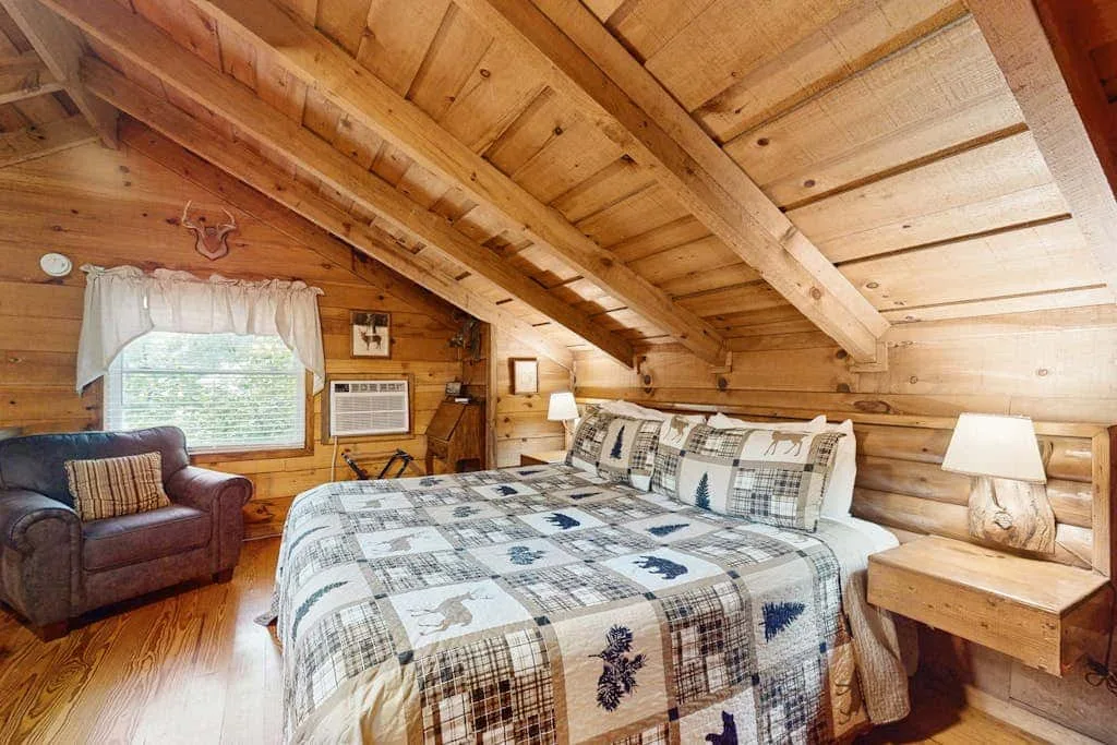 Un dormitorio revestido de madera con una cama y una ventana con vistas a la vegetación.