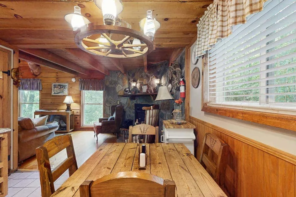 Un comedor con paneles de madera se abre a una sala de estar con chimenea de piedra.