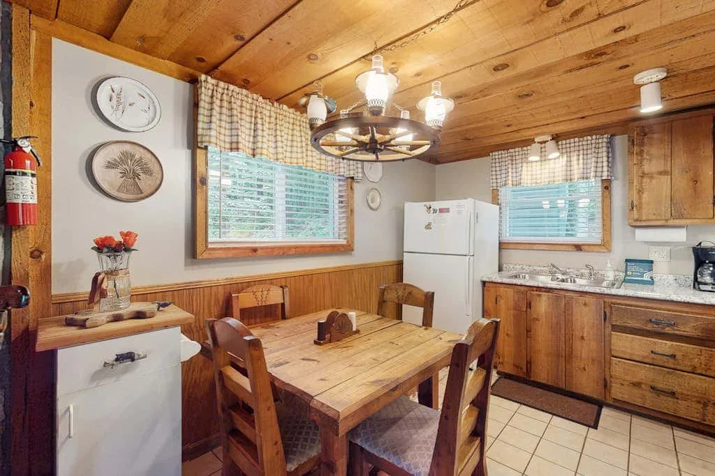 Una cocina y comedor revestidos de madera, con una mesa y un refrigerador.