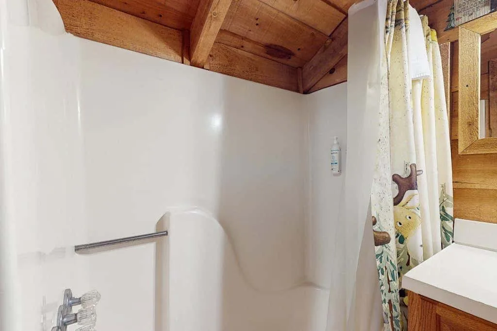 Un baño con ducha, cortina estampada y techo de madera.