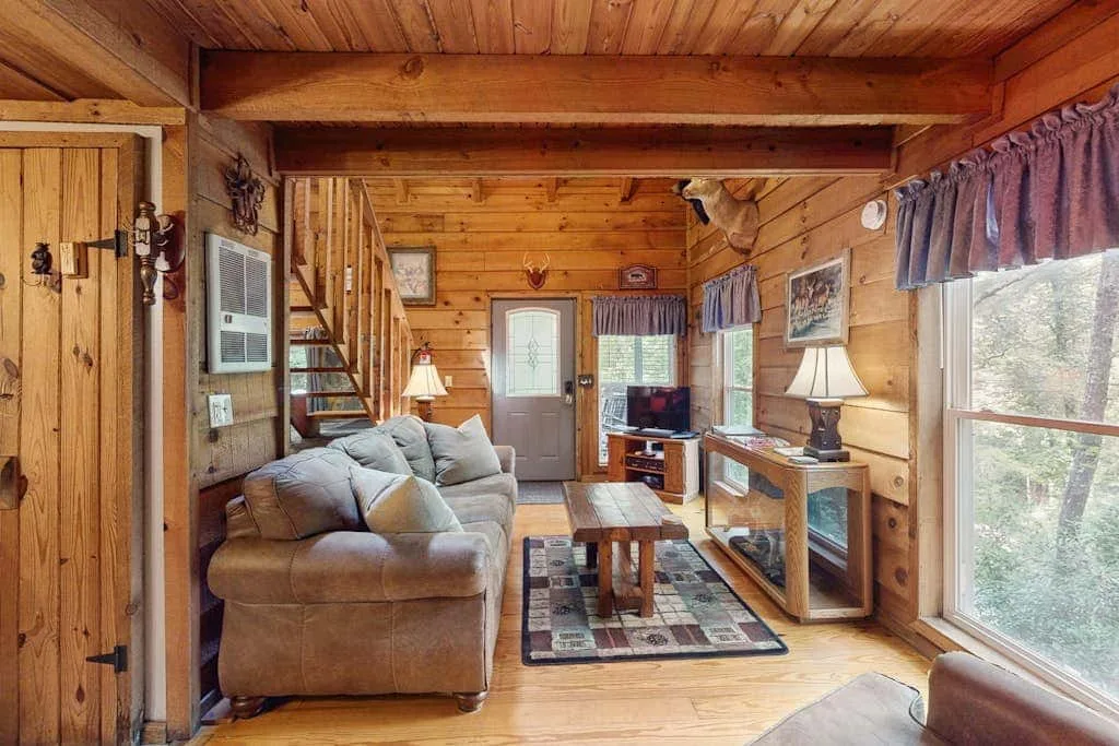 Una sala de estar revestida de madera con asientos, una mesa de centro y ventanas grandes.