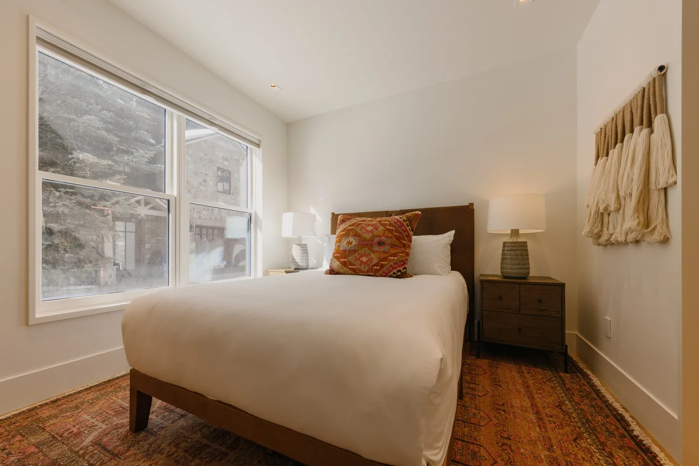 A bedroom with a bed beside large windows and a patterned rug.
