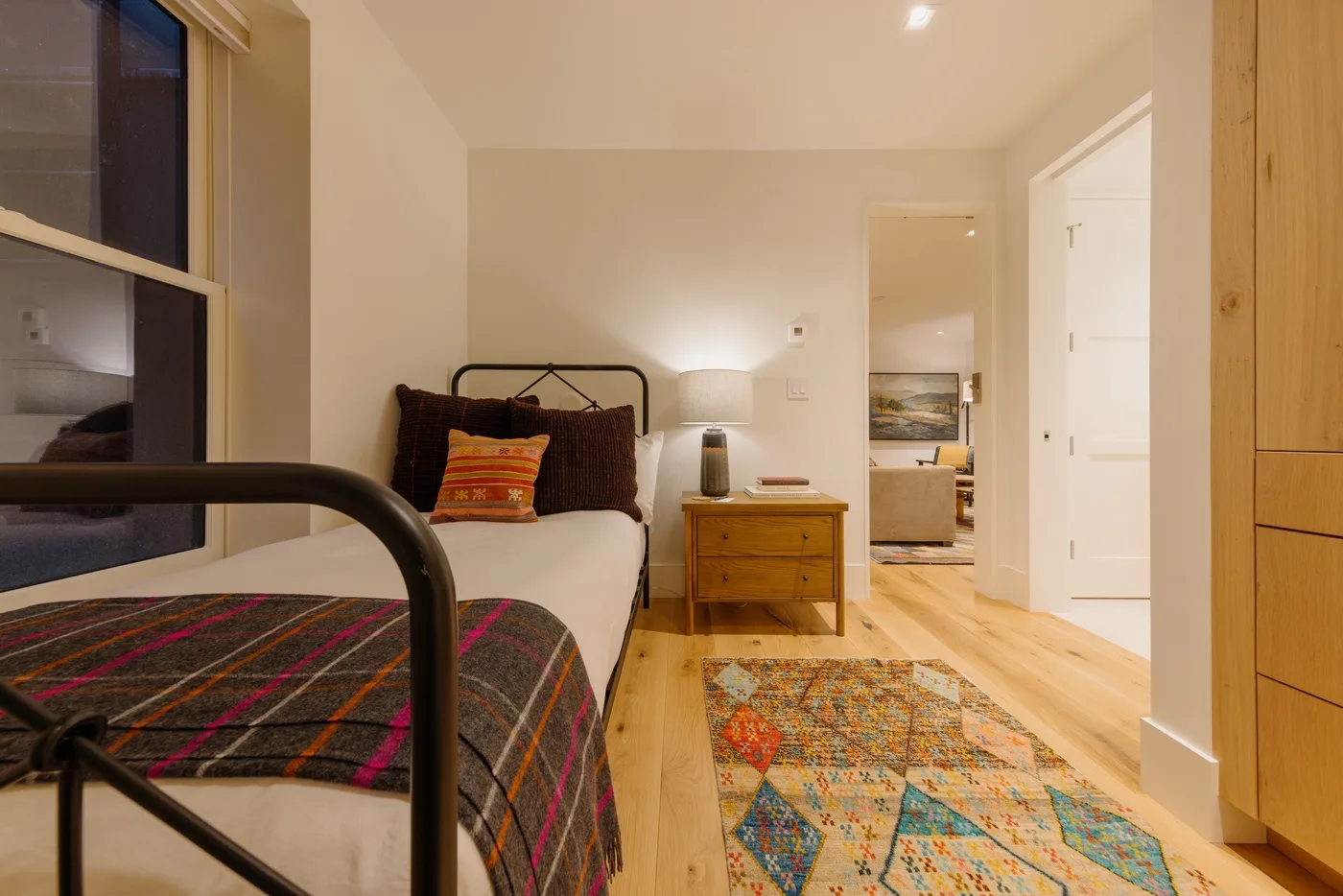 A bedroom with a bed, wooden dresser, and colorful rug.