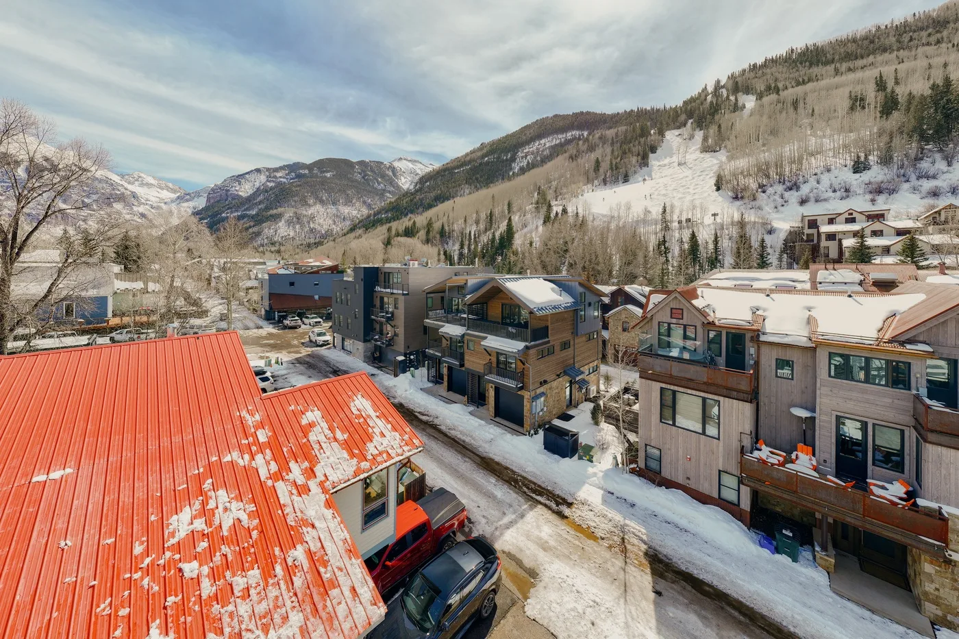 Snowy mountain village with clustered buildings beneath a partly cloudy sky.
