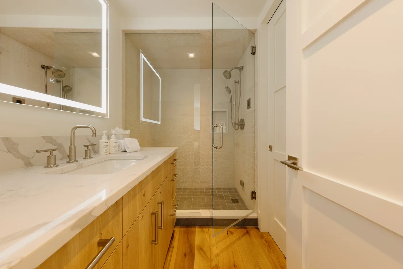 A bright bathroom with a long vanity and glass shower.