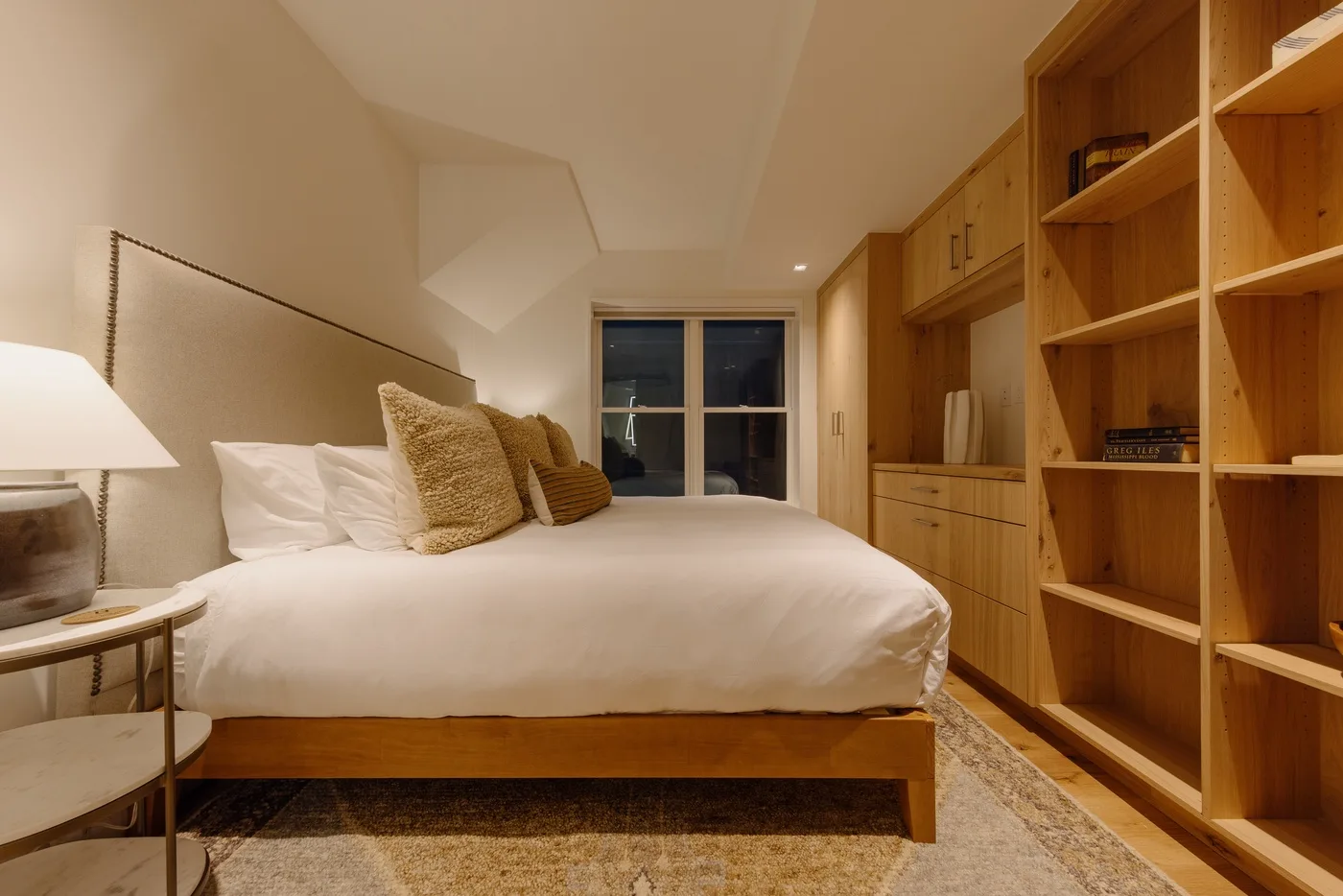 A bedroom with a bed beside built-in wooden shelving.