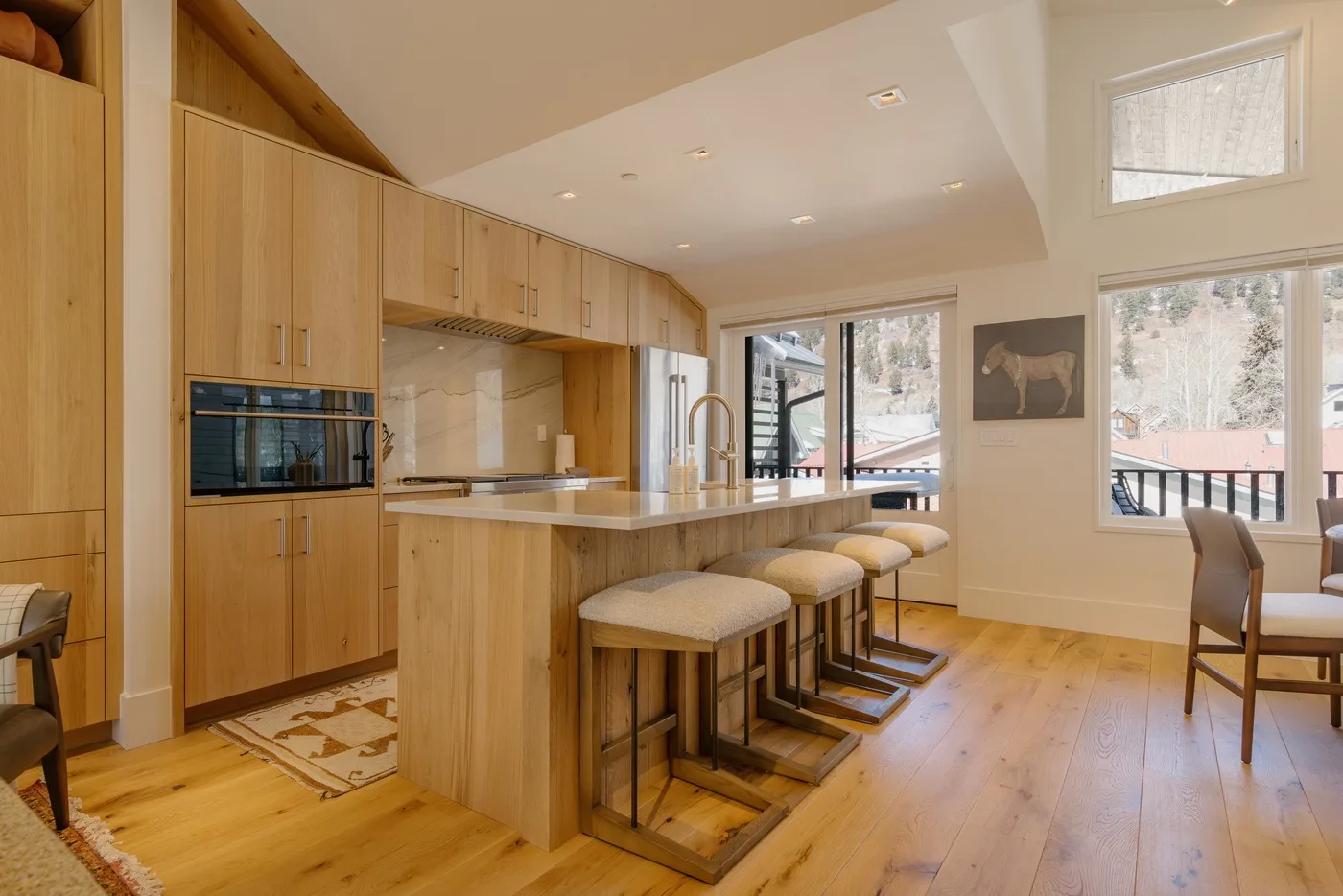 A bright kitchen with a long island and seating beside large windows.