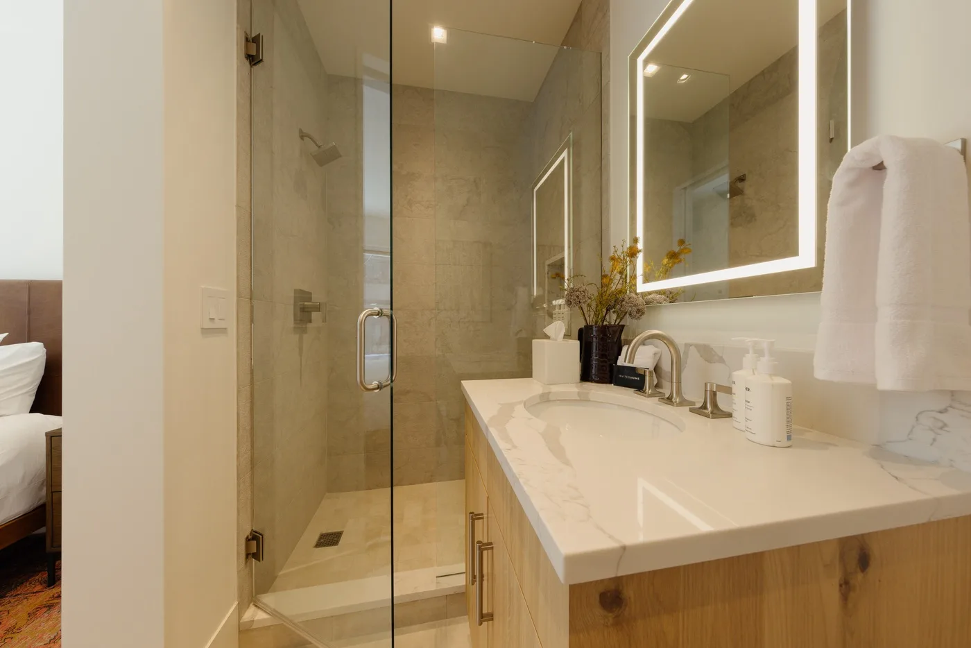 A modern bathroom with a glass shower and a long vanity beneath a lit mirror.