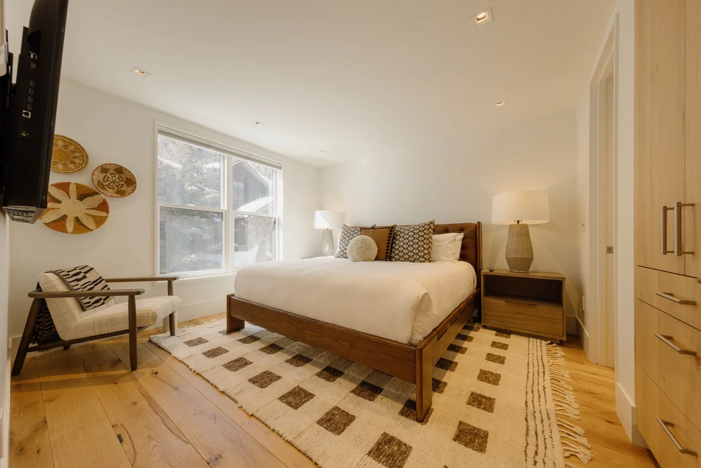 A bedroom with a wooden bed, patterned rug, and large window.