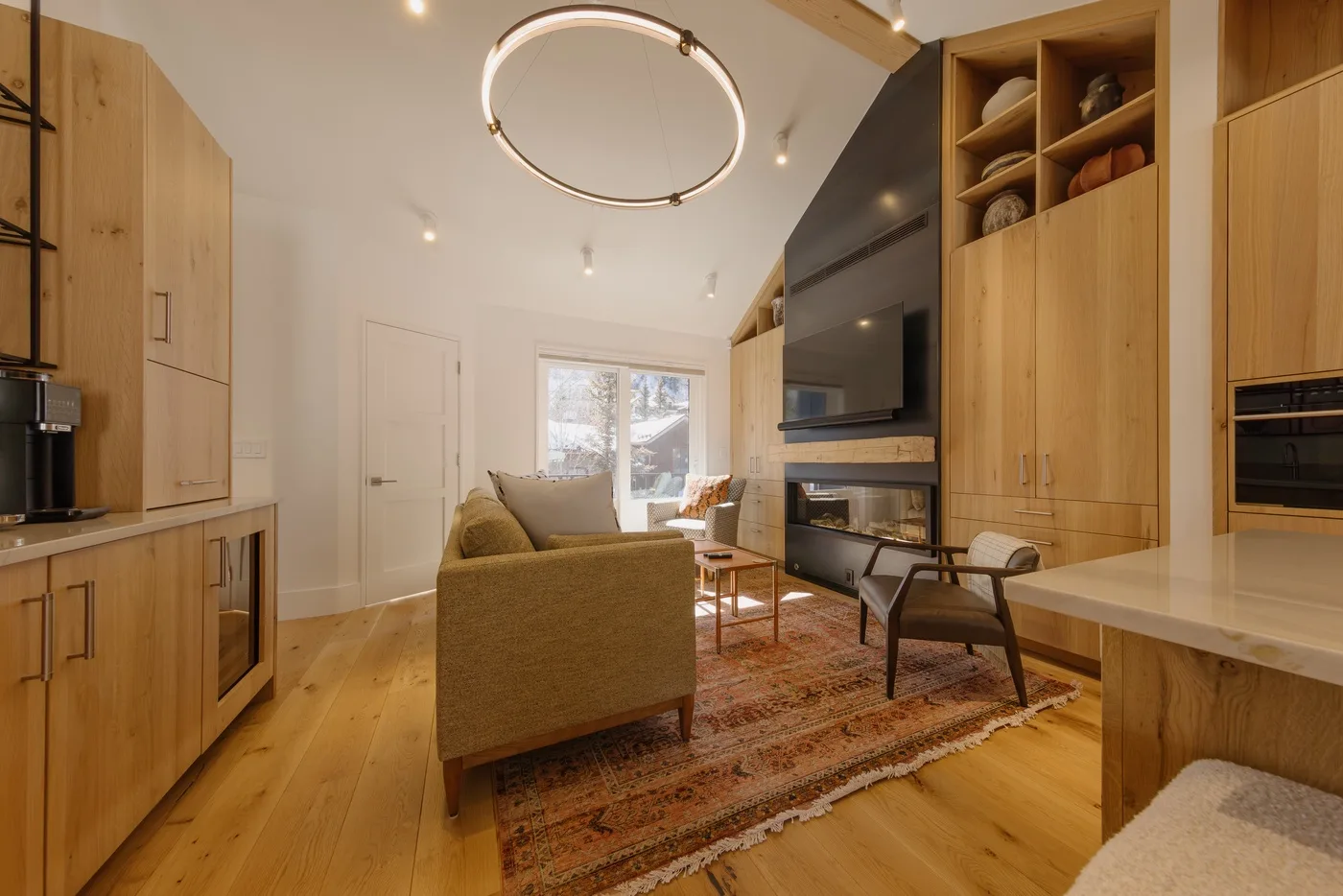 A warm-toned living room with seating arranged around a rug and a large television.