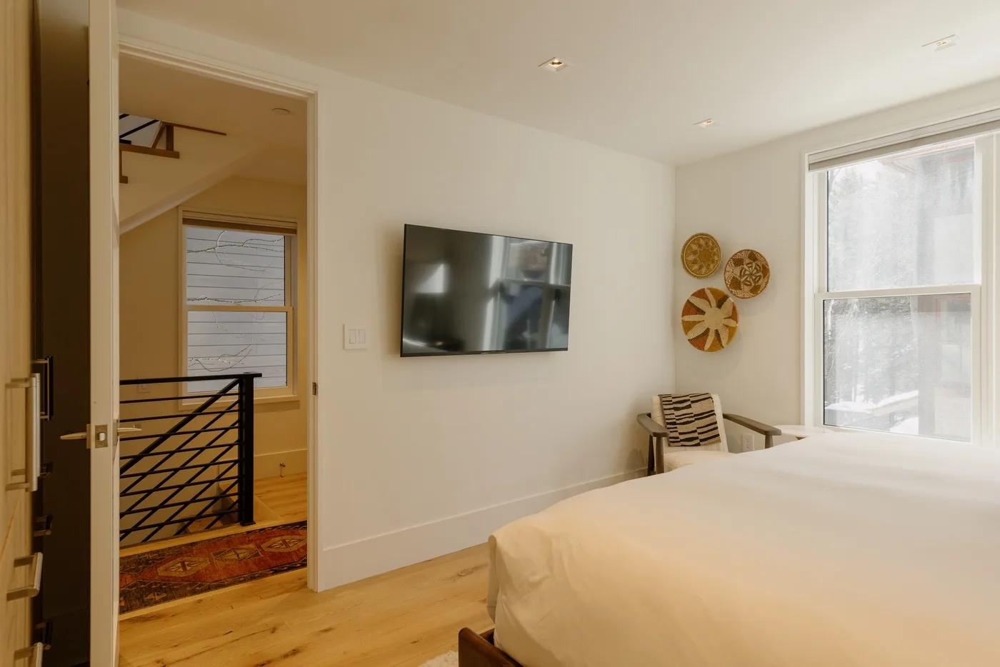 A bedroom with a wall-mounted television and a large window.