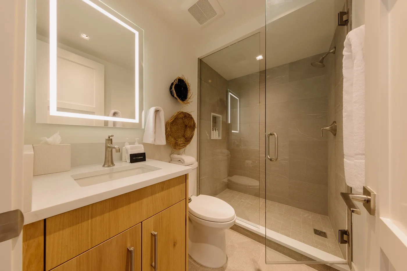 A bathroom with a vanity, illuminated mirror, toilet, and glass shower.