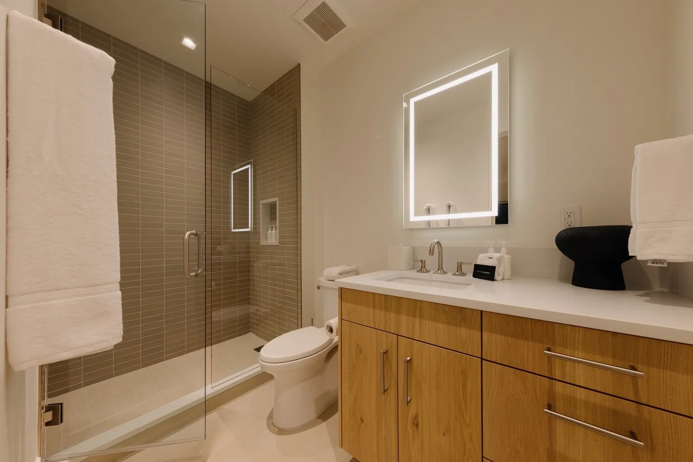 A bathroom with a glass shower, toilet, and wood-front vanity.