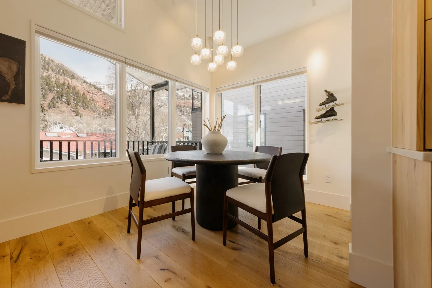 A dining area with a dark table and chairs beside large windows.