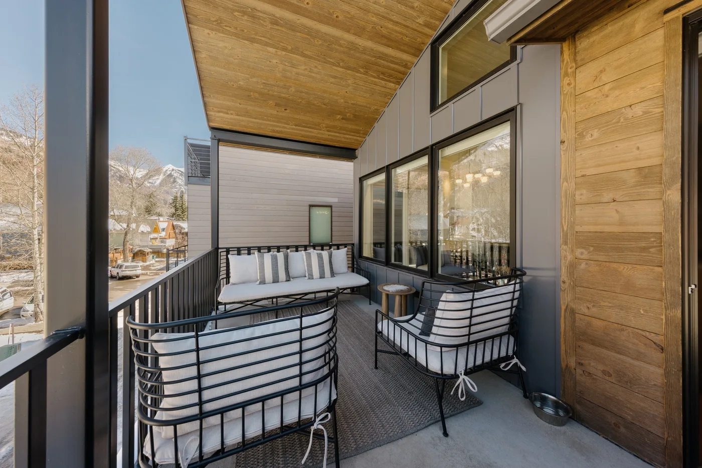 A covered balcony has seating beside large windows and a wood-paneled wall.