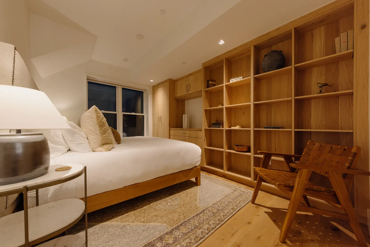 A bedroom with a bed, wooden shelving, and a seating area.